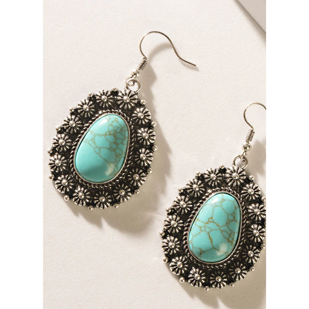 Turquoise earrings with silver floral designs on a light background