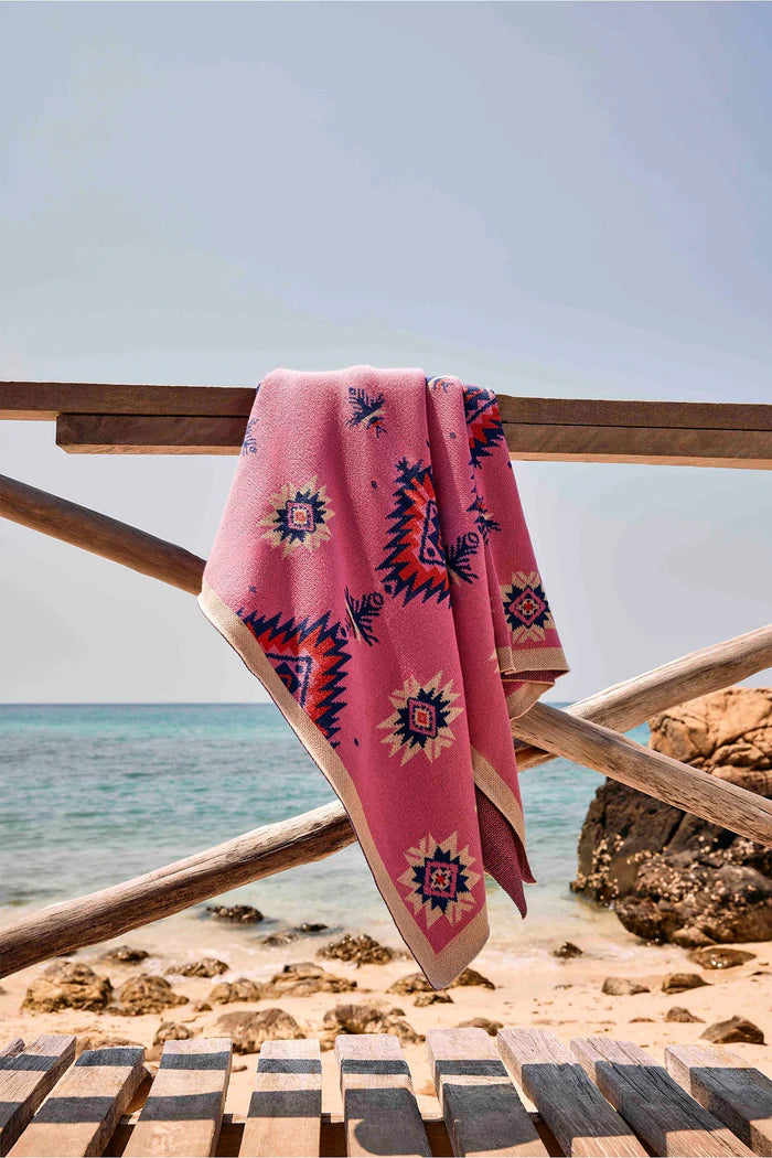 Pink towel with geometric patterns draped over a wooden railing by the beach.