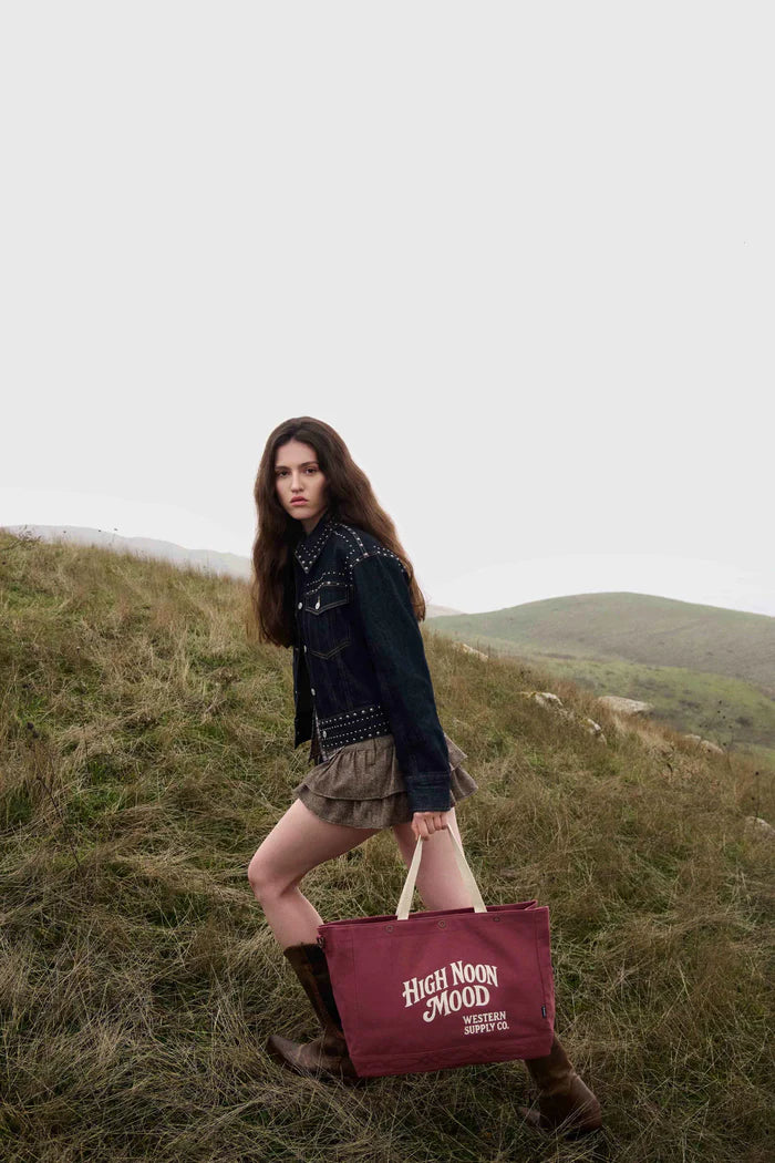 Woman holding a 'High Noon Mood' bag in a grassy field