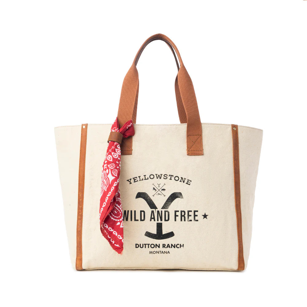 Yellowstone Ivory Creek Weekender Bag with Scarf. Canvas tote bag with brown handles and a red bandana, featuring 'Yellowstone Wild and Free' text on a white background.