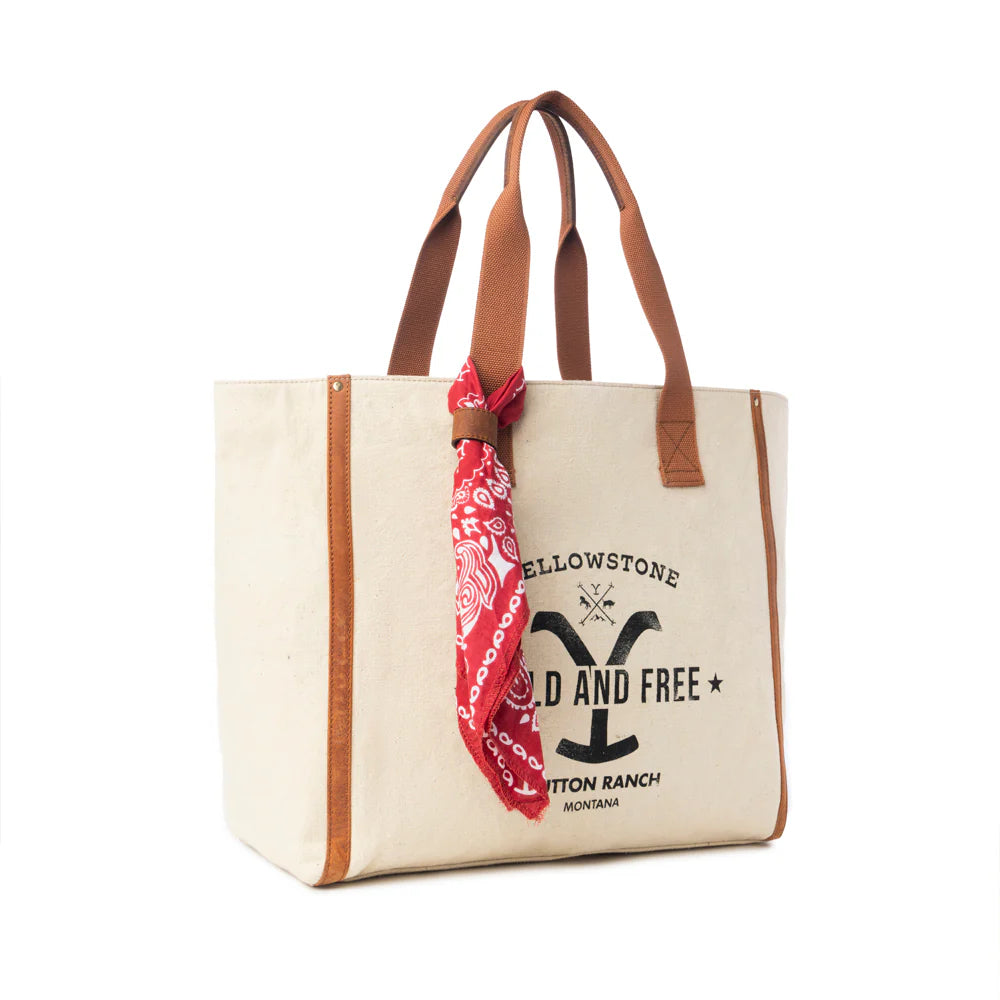 Yellowstone Ivory Creek Weekender Bag with Scarf. Beige tote bag with brown handles and a red bandana, featuring 'Yellowstone' branding.