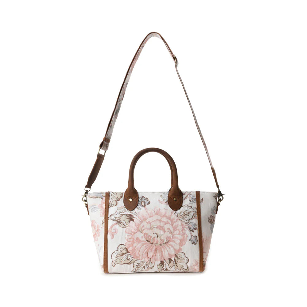 Floral patterned handbag with brown handles and strap on a white background
