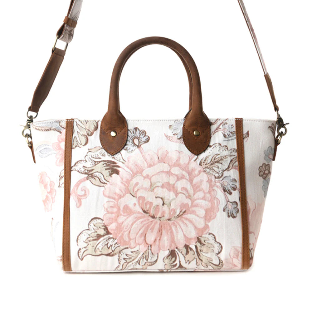 Floral patterned handbag with brown handles and strap on a white background