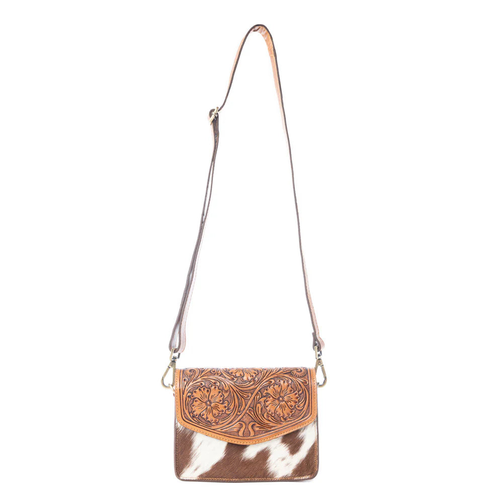 Bridle Blossom Handtooled Hairon Leather Bag in Amber Carve. Cowhide crossbody bag with decorative flap on a white background