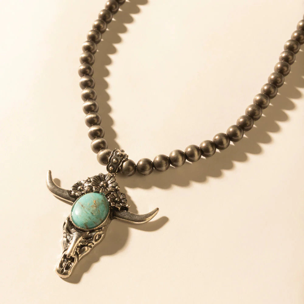 Necklace with bull head pendant and turquoise stone on a beige background