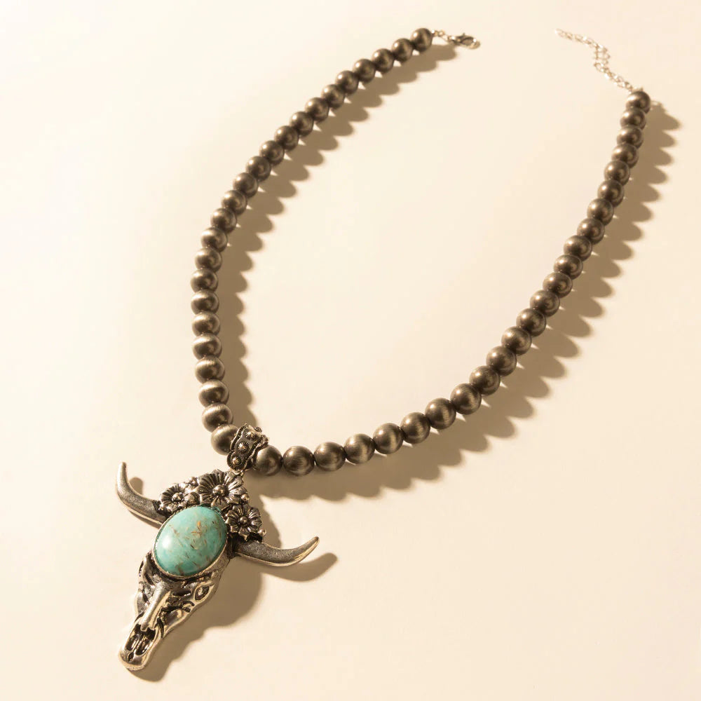 Necklace with bull skull pendant and turquoise stone on a beige background