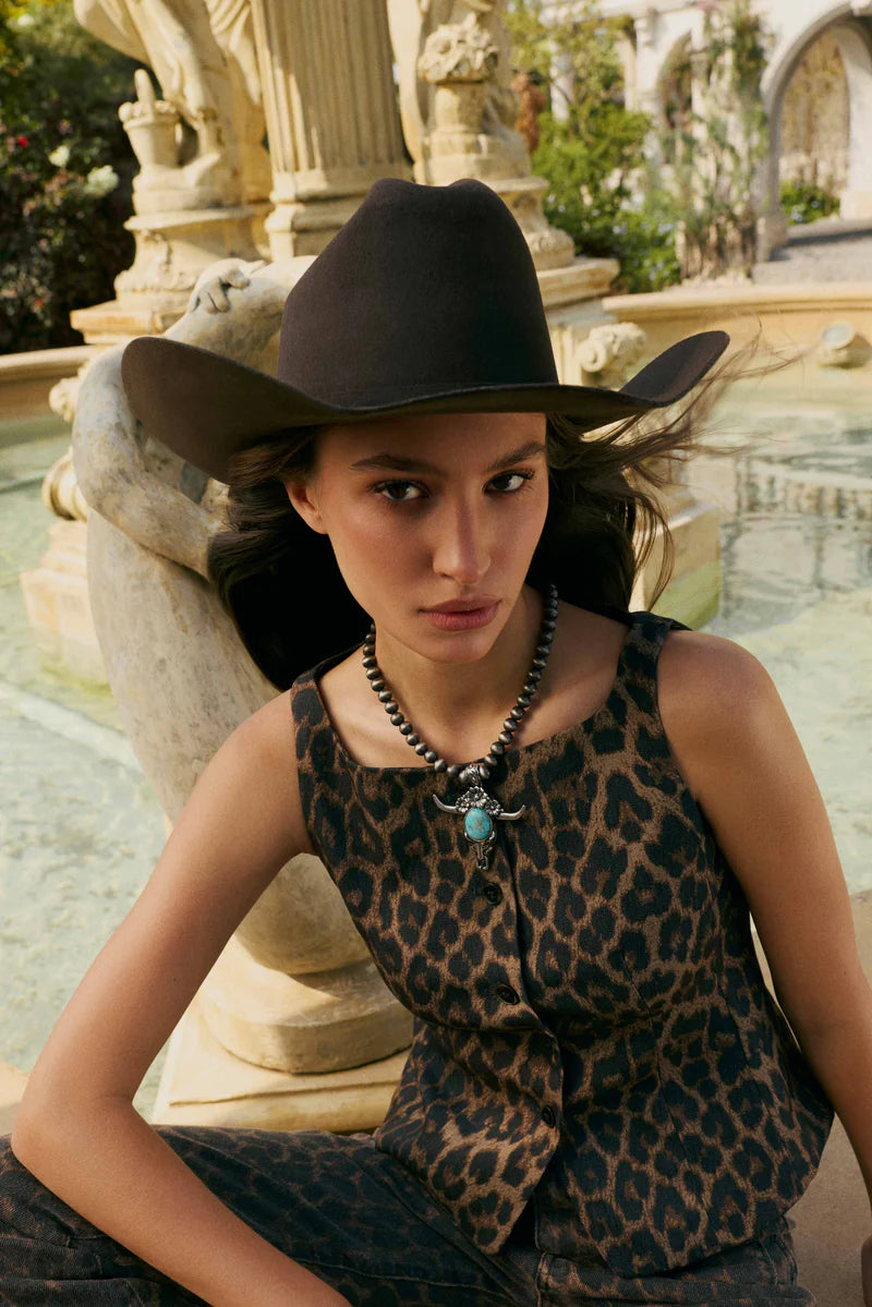 Woman wearing a leopard print top and black cowboy hat sitting by a fountain.