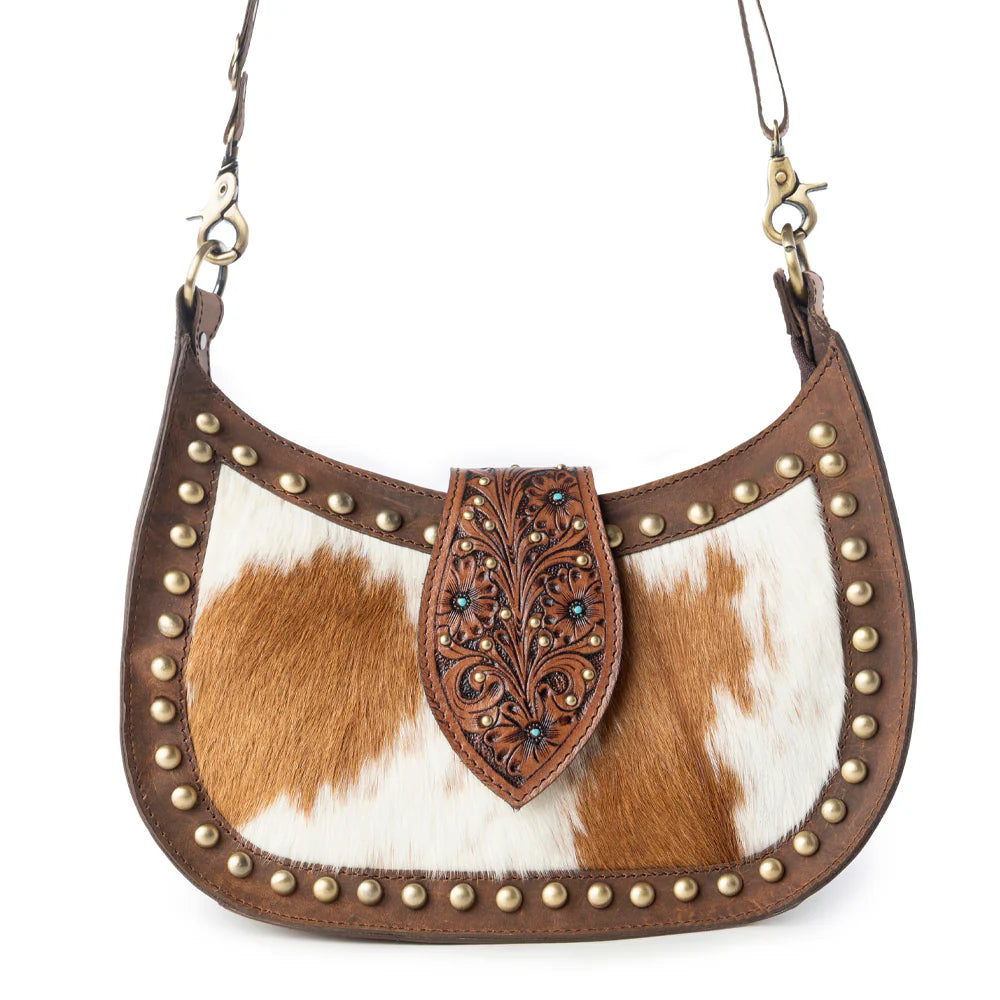 Brown and white cowhide handbag with decorative flap and studs on a white background