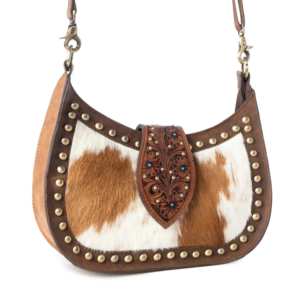 Brown and white cowhide handbag with decorative studs and leather flap on a white background