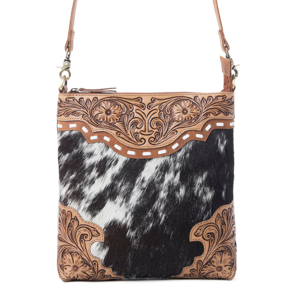 Cowhide patterned handbag with intricate brown leather tooling on a white background