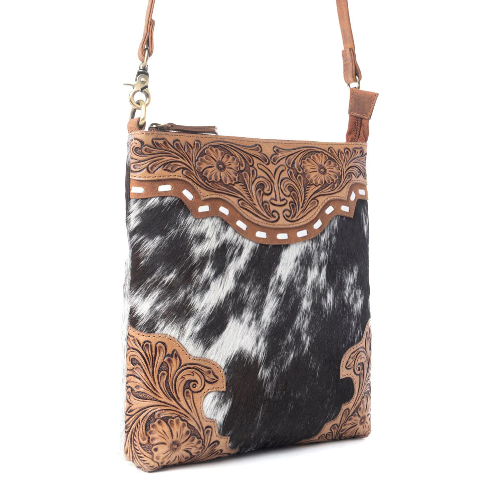 Cowhide patterned handbag with intricate brown leather tooling on a white background