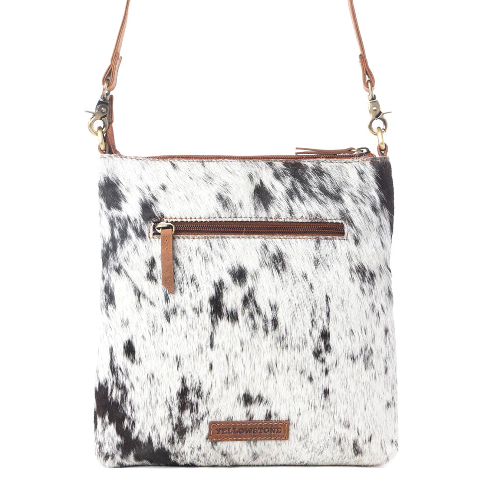 Cow print crossbody bag with brown accents on a white background