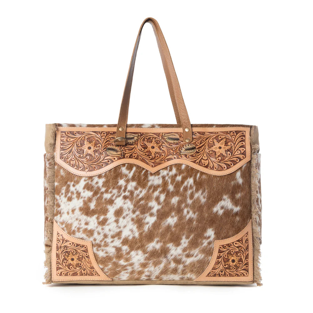 Tote bag with cowhide pattern and intricate leather accents on a white background