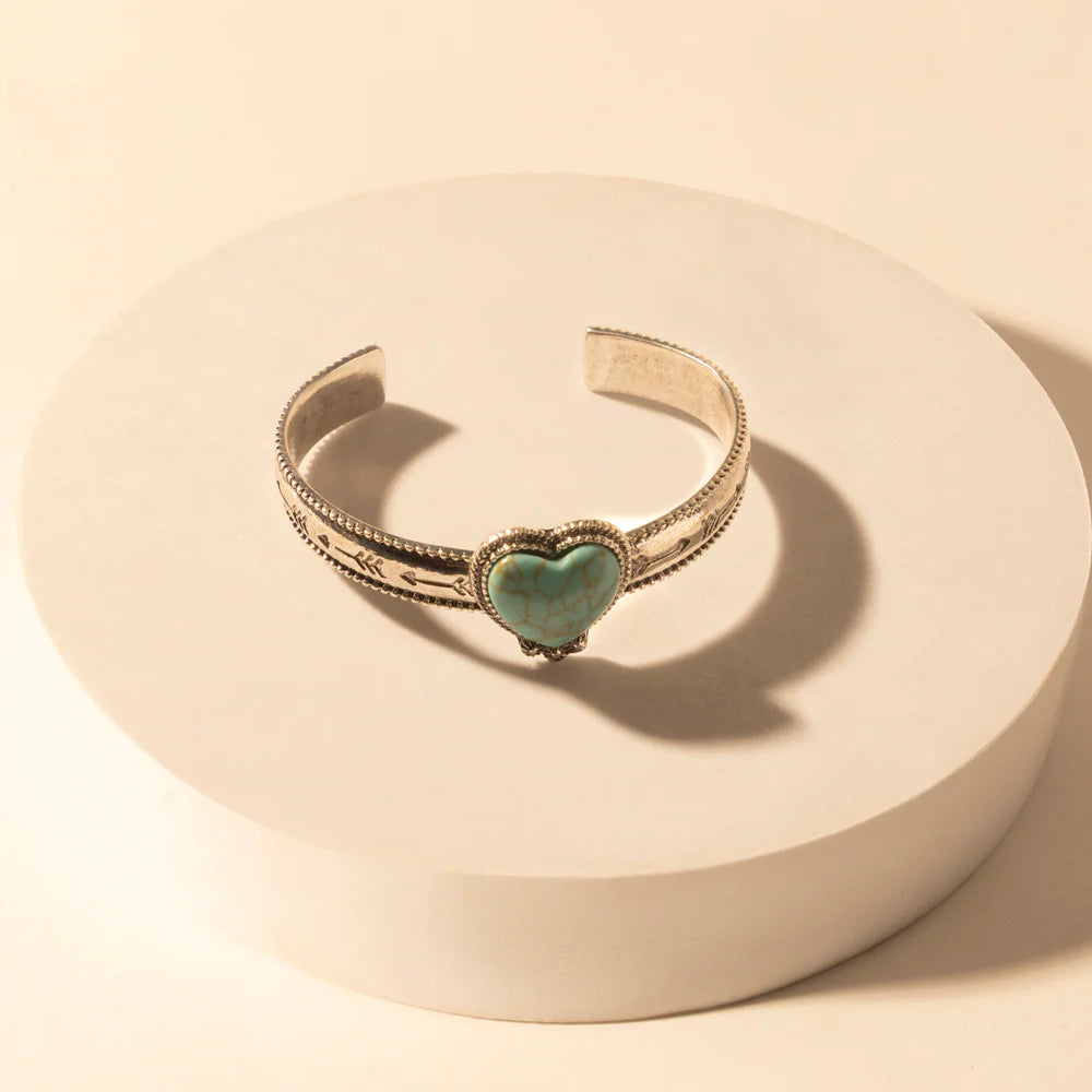 Gold bracelet with a heart-shaped turquoise stone on a beige background