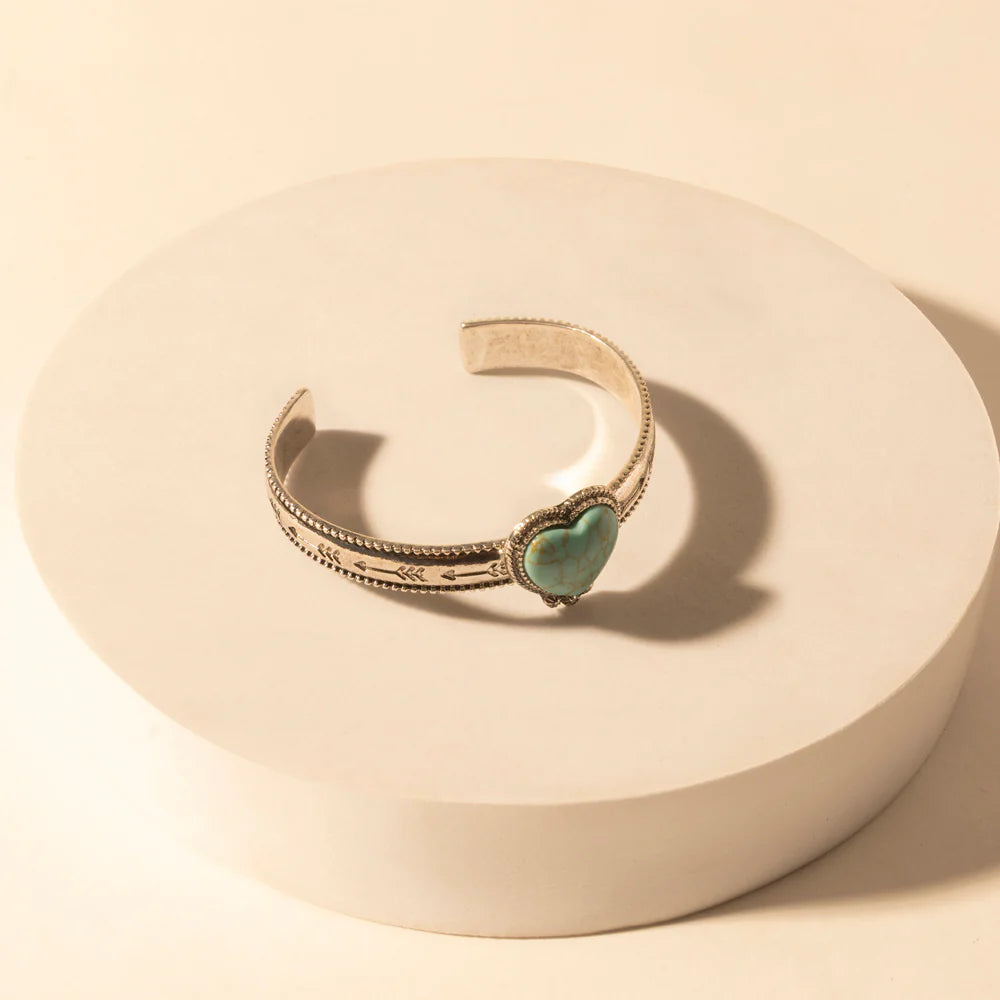 Gold bracelet with a heart-shaped turquoise stone on a beige background