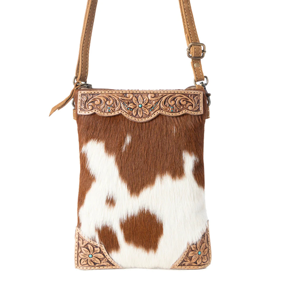 Brown and white cowhide leather crossbody bag with decorative metal trim on a white background
