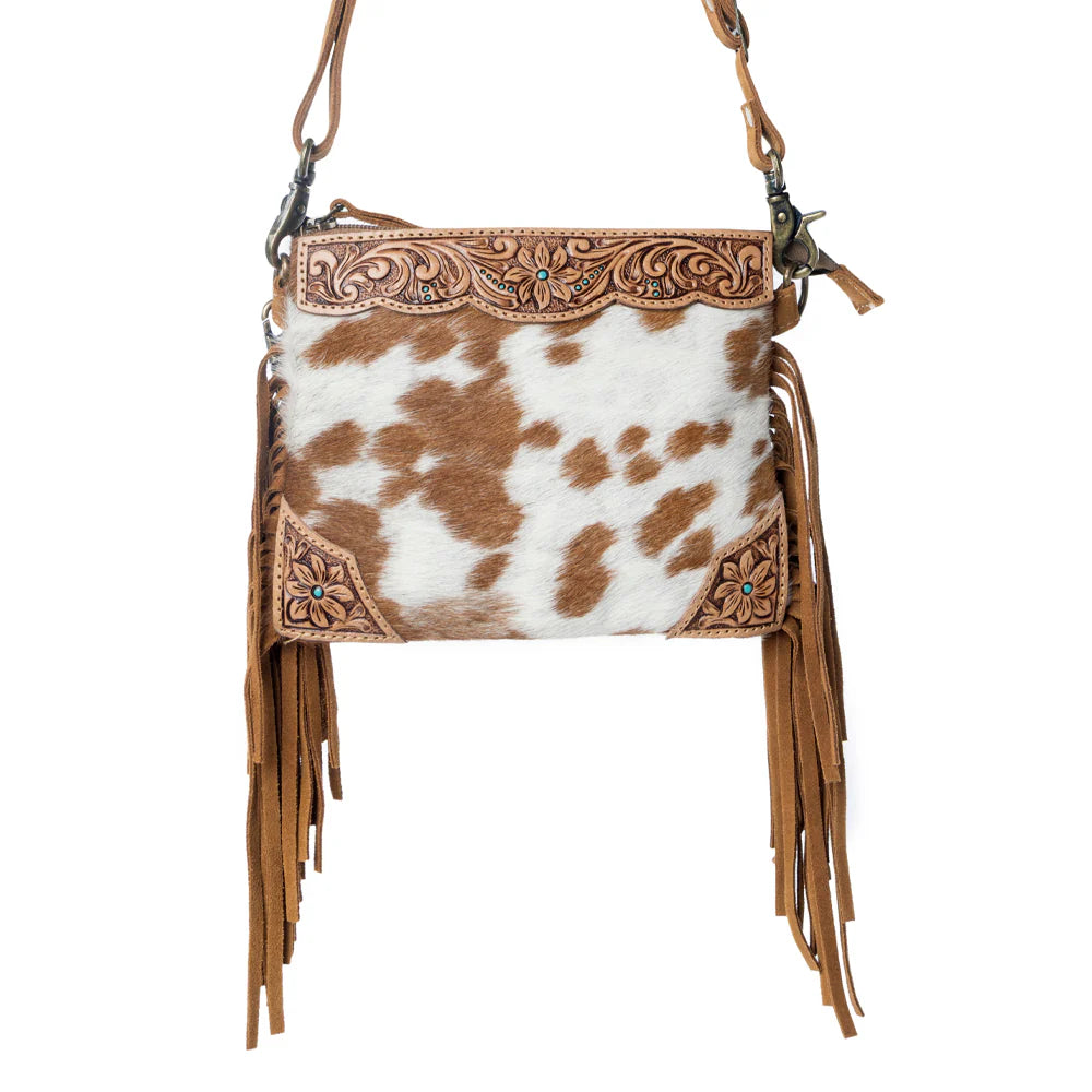 Cowhide leather handbag with fringe and intricate tooling on a white background