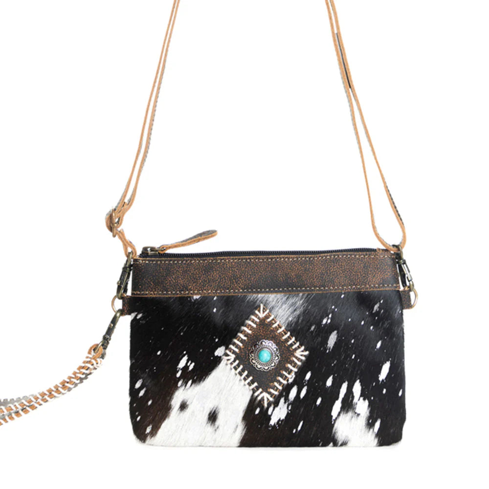 Eye of the Goddess Crossbody Bag in Black. Black and white cowhide handbag with a decorative element on a white background