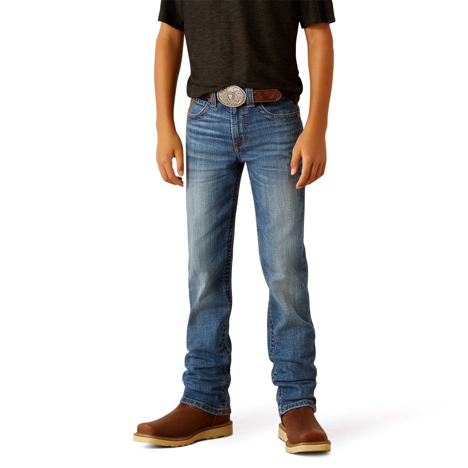 Ariat Boy's B5 Norwich Slim Fit Jean. A boy standing, wearing blue slim fit jeans and brown shoes.