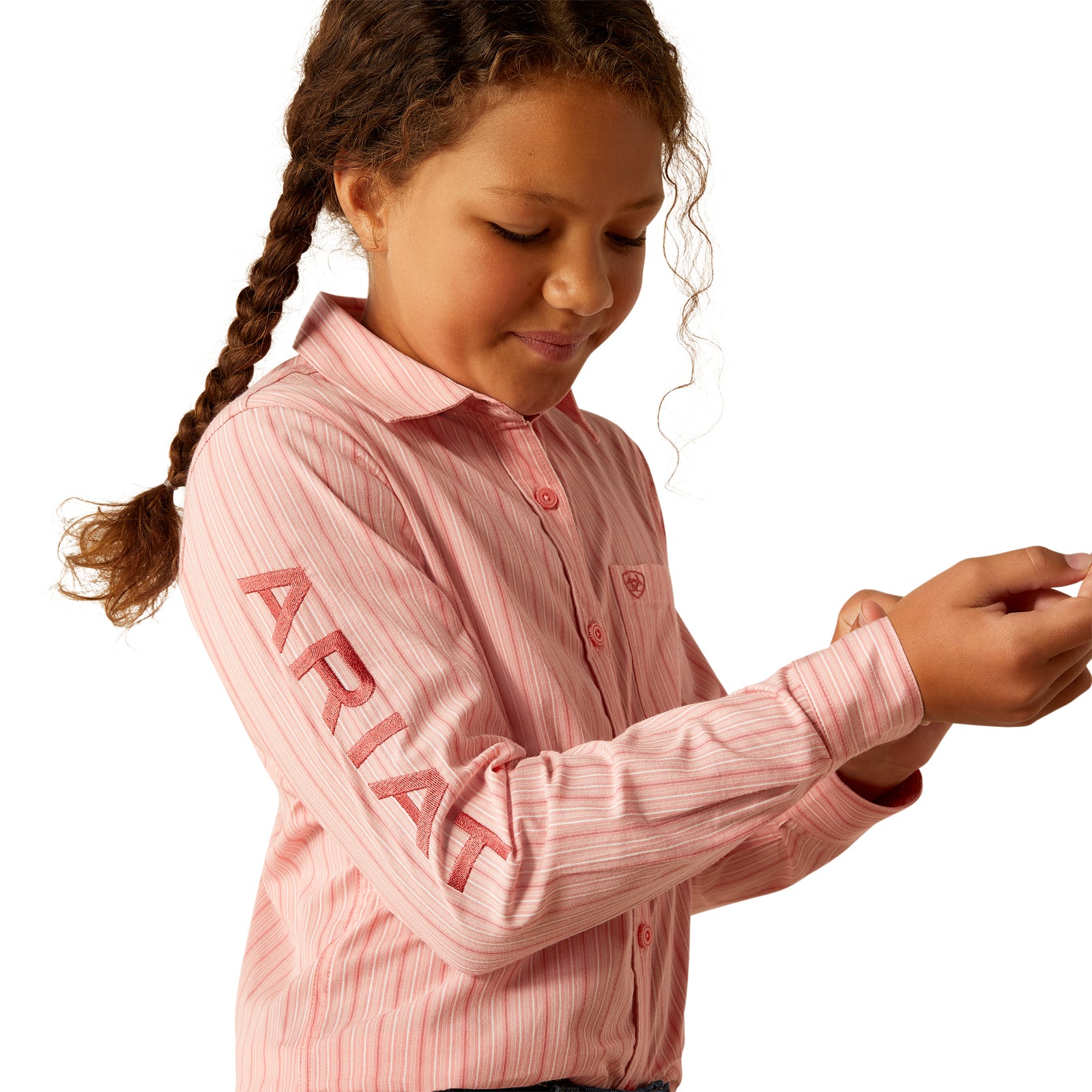 Ariat Girl's Team Kirby L/S Western Shirt. Young girl wearing a pink shirt with 'Ariat' branding on a white background