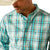 Ariat Men's Pro Series Justice Classic Fit L/S Shirt. Man wearing a plaid shirt, jeans, and a cowboy hat on a white background