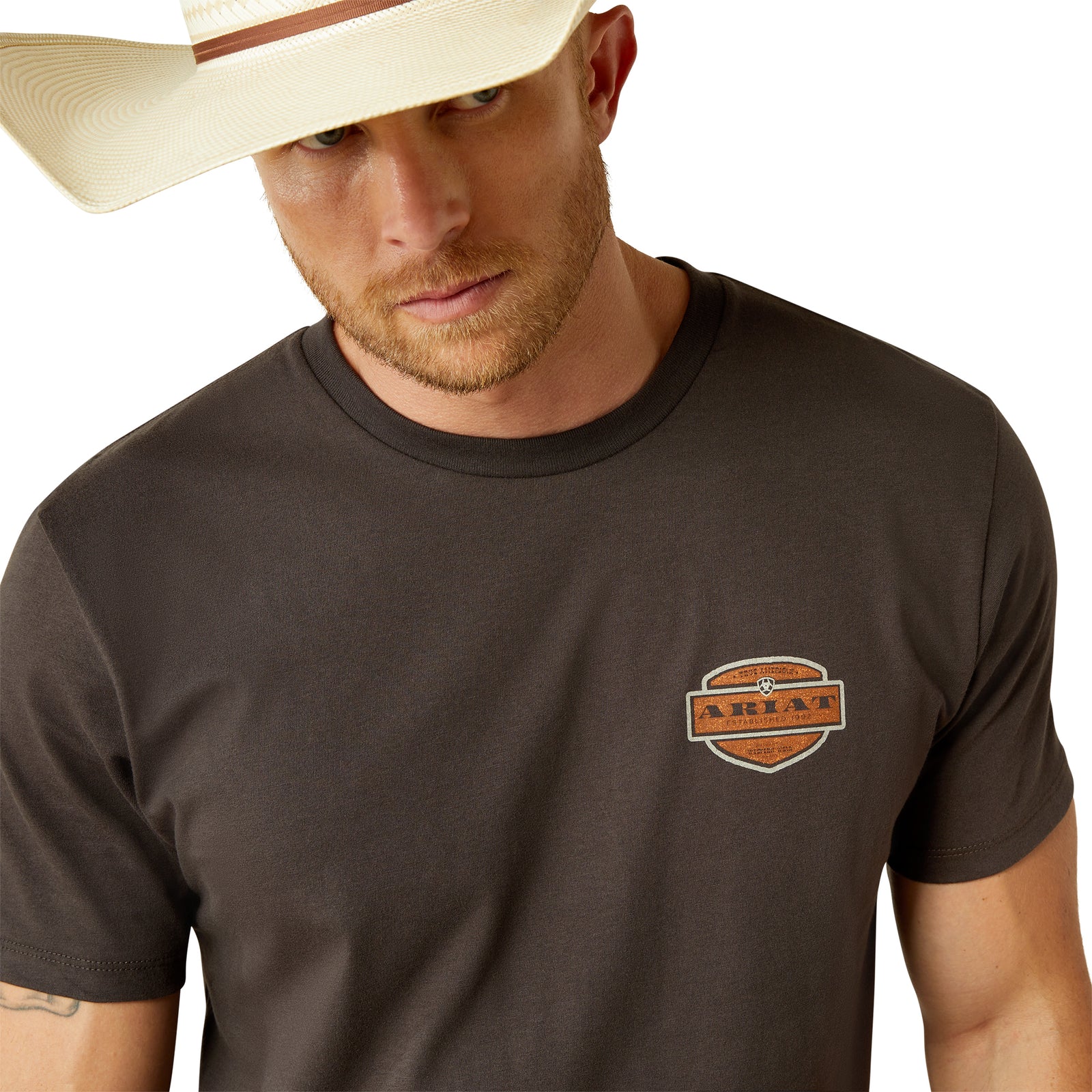 Ariat Men's Ol' Style Lockup T-Shirt. Man wearing a brown t-shirt with a logo and a straw hat on a white background