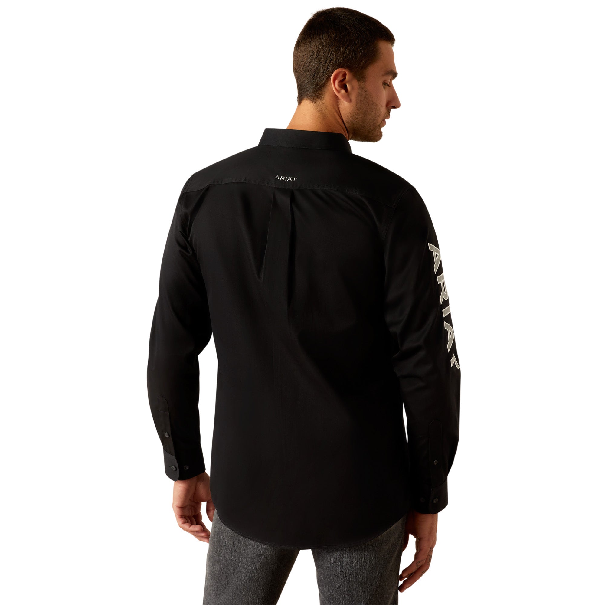 Ariat Men's Team Logo Twill L/S Western Shirt. Man wearing a black Ariat shirt, gray jeans, and a cowboy hat on a white background