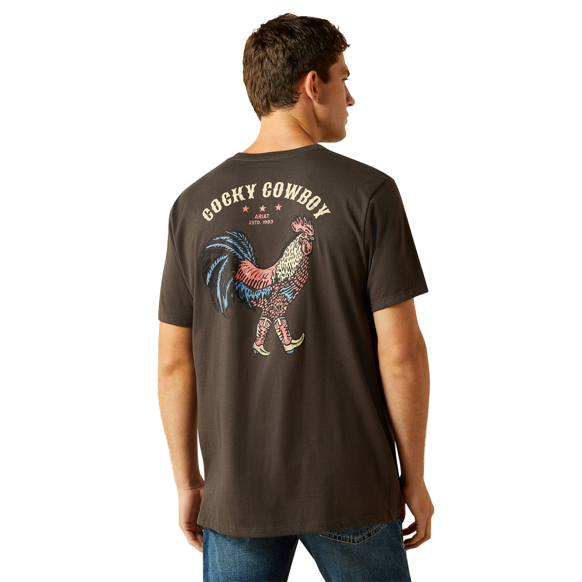 Ariat Men&#39;s Cowboy Cocky T-Shirt. Man wearing a dark brown t-shirt with a colorful rooster graphic and &#39;Cocky Cowboy&#39; text on the back.