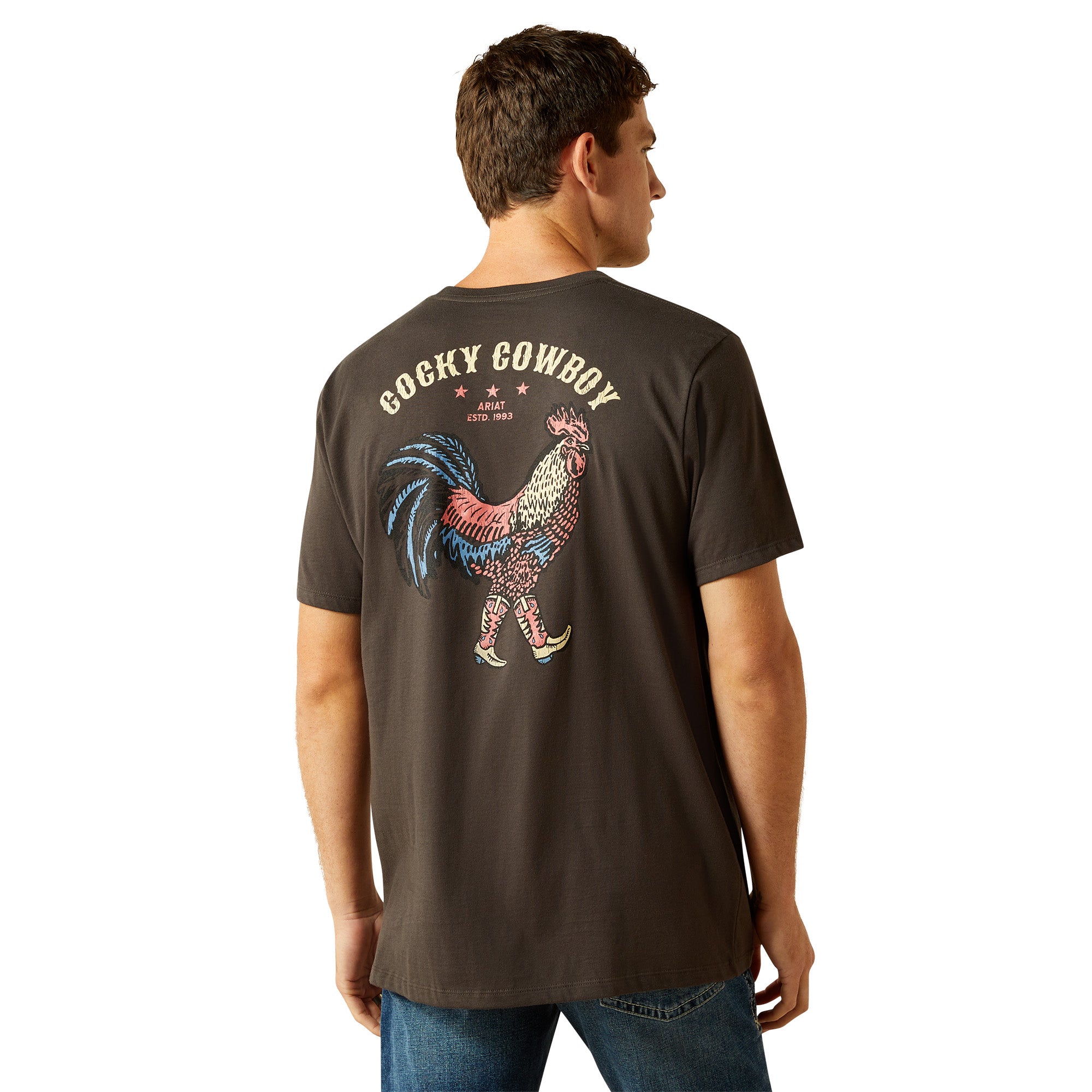 Ariat Men's Cowboy Cocky T-Shirt. Man wearing a dark brown t-shirt with a colorful rooster graphic and 'Cocky Cowboy' text on the back.