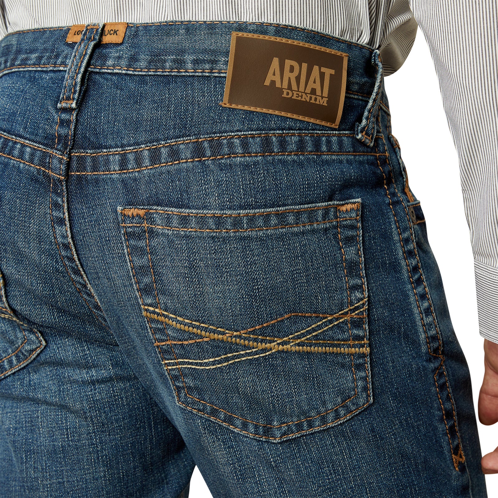 Ariat Men's M4 Norwich Relaxed Fit Jean. Close-up of blue jeans with Ariat denim label on a white background
