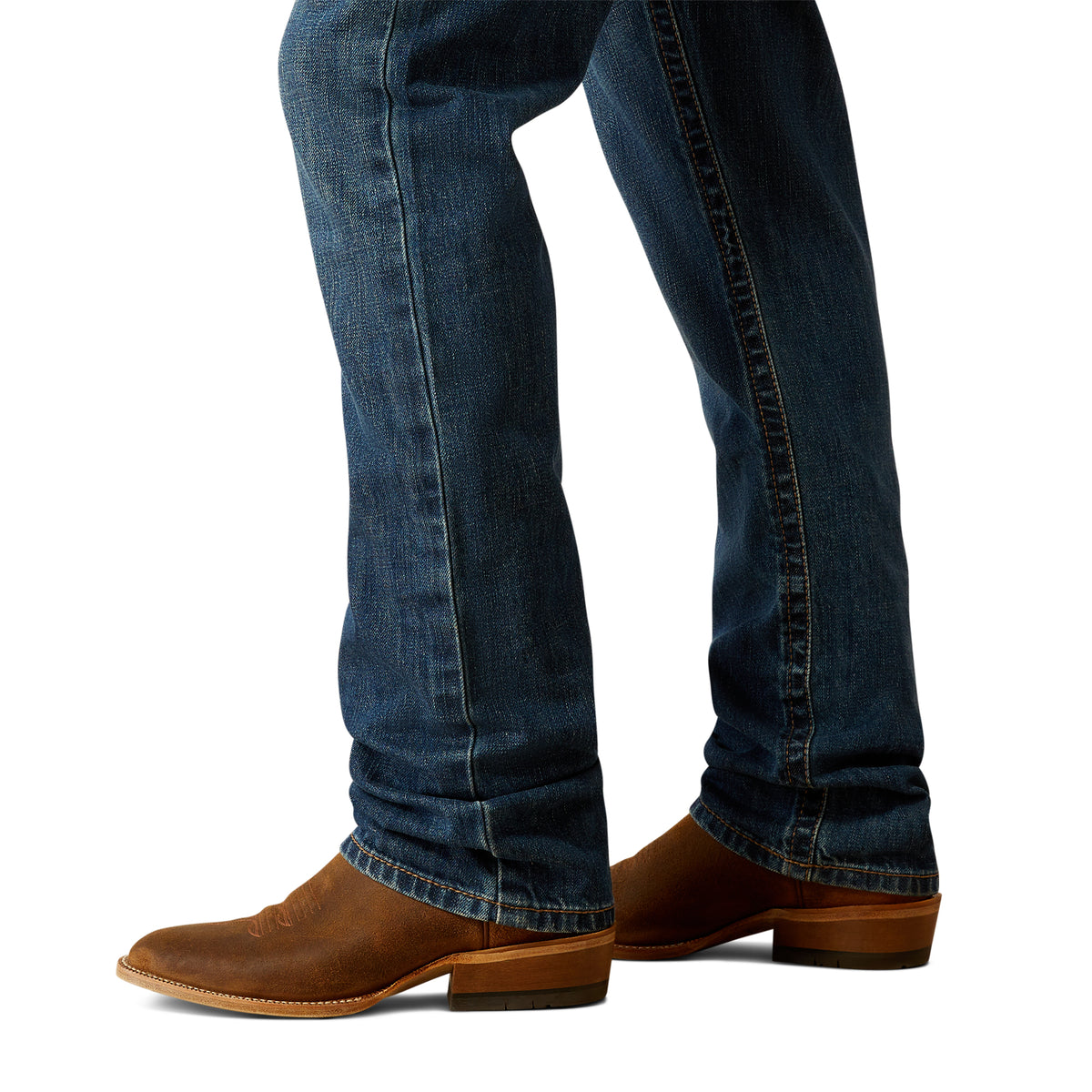 Ariat Men's M4 Norwich Relaxed Fit Jean. Blue jeans worn with brown boots on a white background