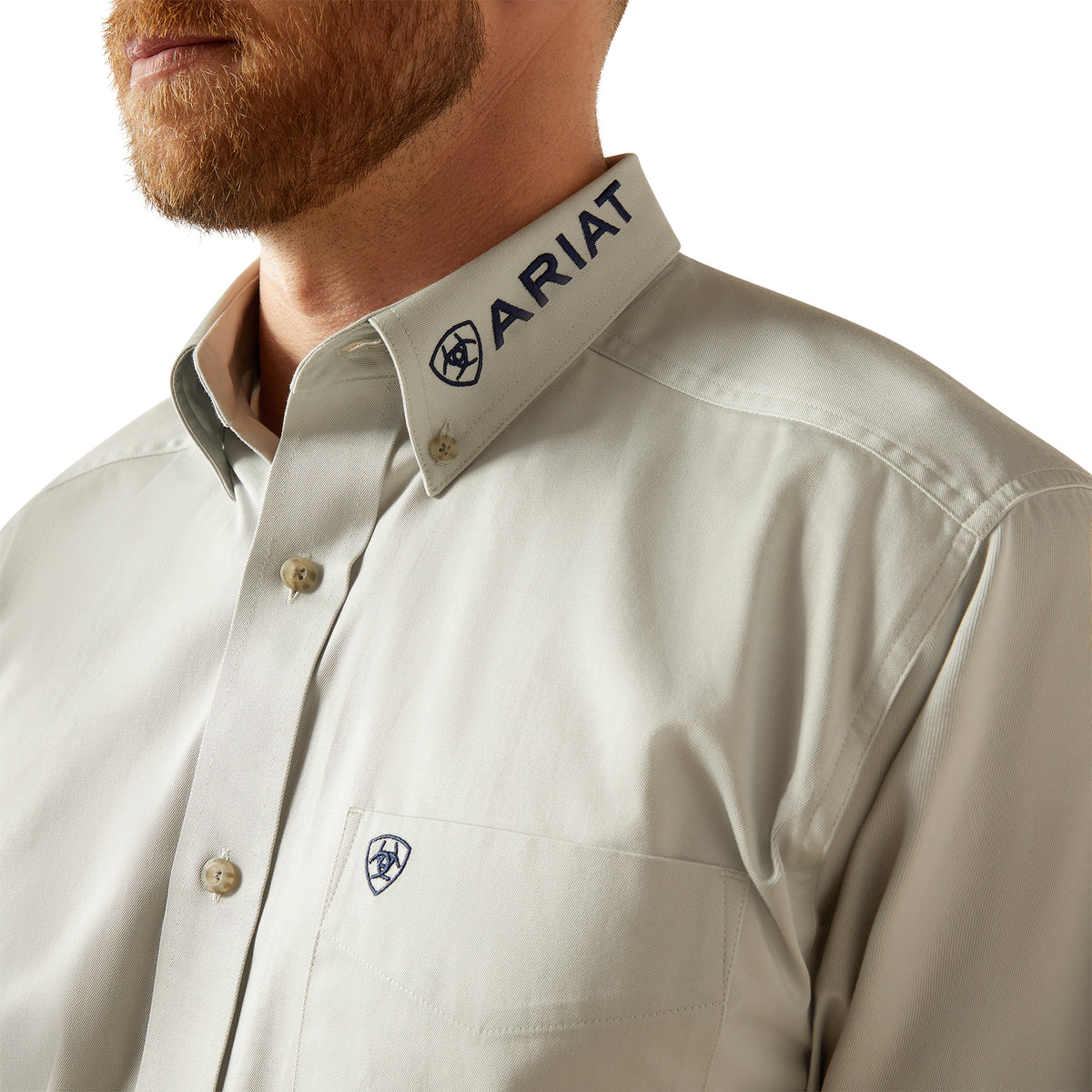 Ariat Men's Team Logo Twill L/S Western Shirt. Close-up of a beige shirt with Ariat logo on a white background