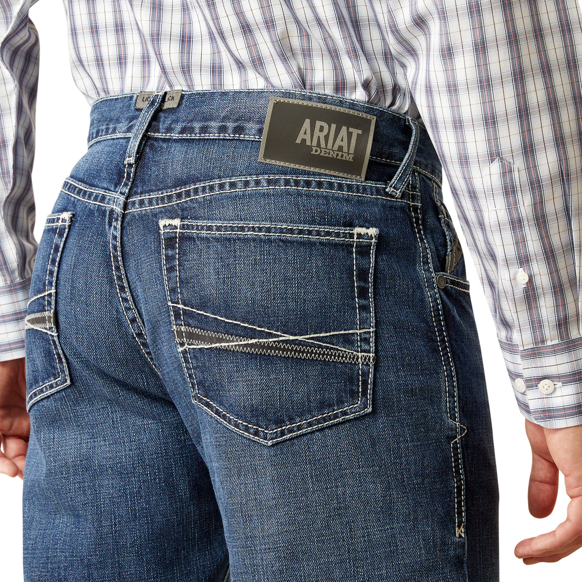 Ariat Men's M2 Camilo Boot Cut Jean. Close-up of blue jeans with Ariat logo on the back pocket, worn by a person.