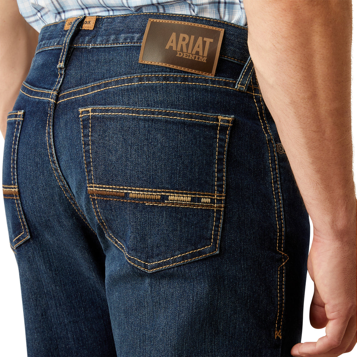 Ariat Men's M4 Otis Boot Cut Jean. Close-up of blue jeans with Ariat denim label on a white background
