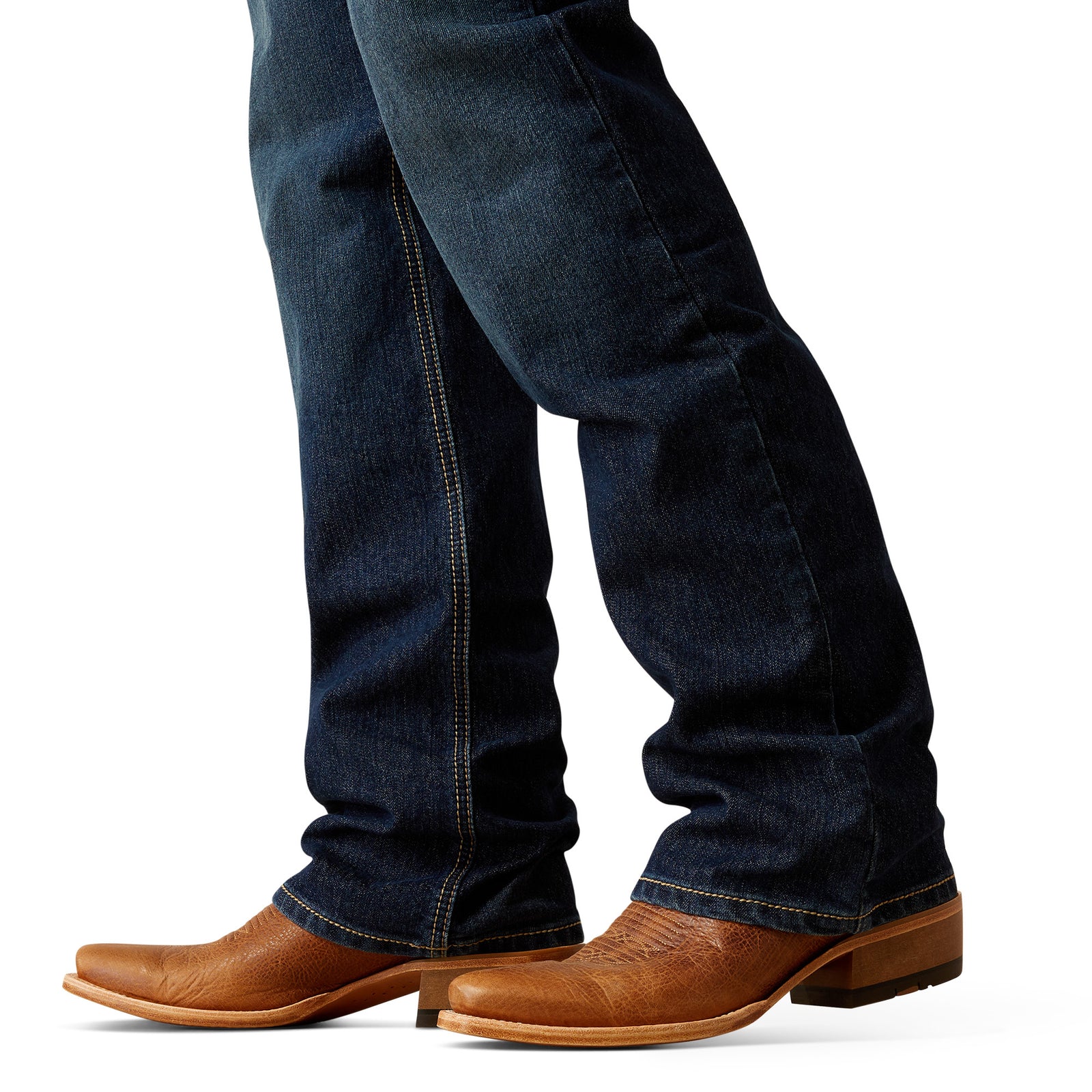 Ariat Men's M4 Otis Boot Cut Jean. Dark blue jeans worn with brown leather boots on a white background