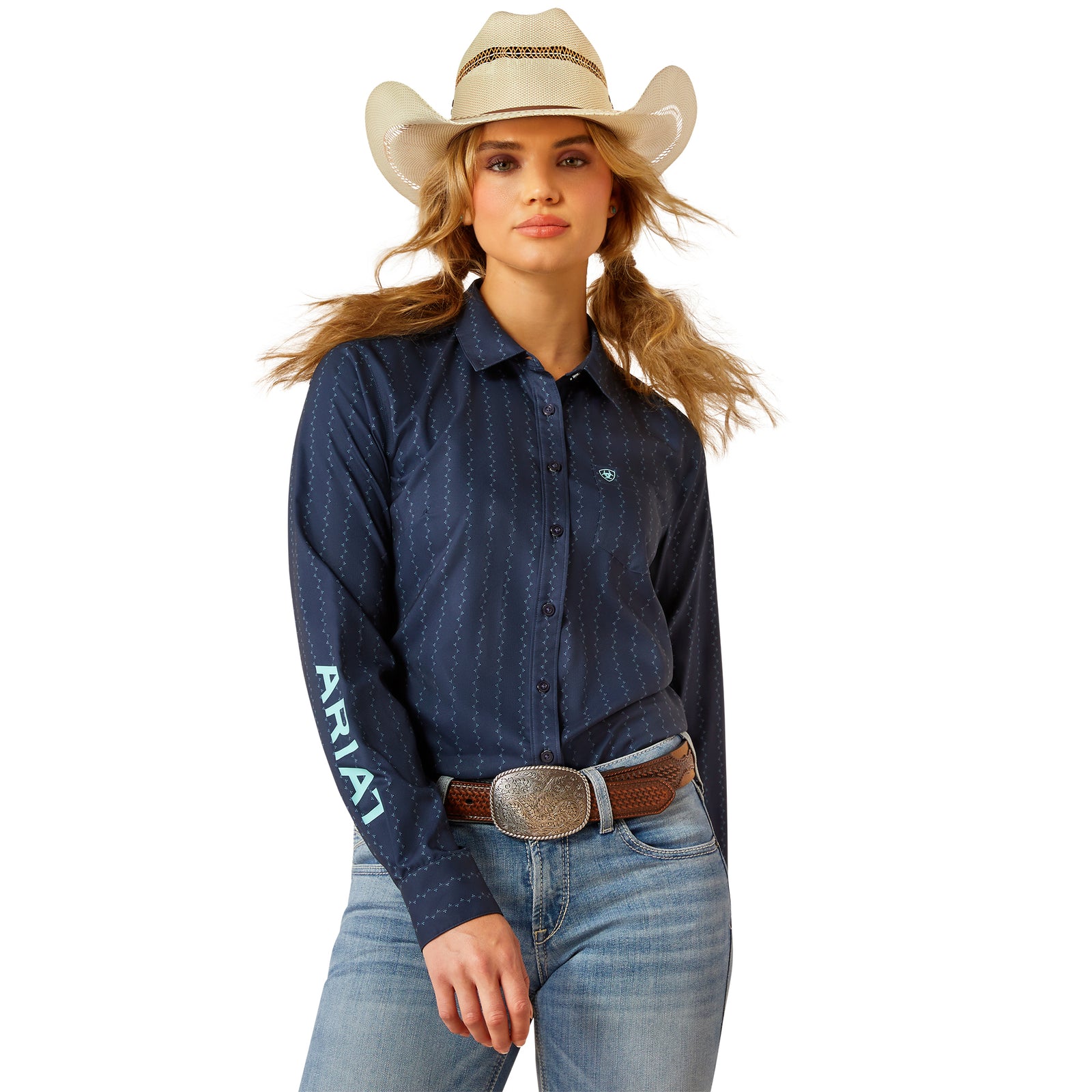 Ariat Women's Kirby Pro L/S Western Shirt. Woman wearing a blue denim shirt with 'Ariat' branding, jeans, and a cowboy hat on a white background