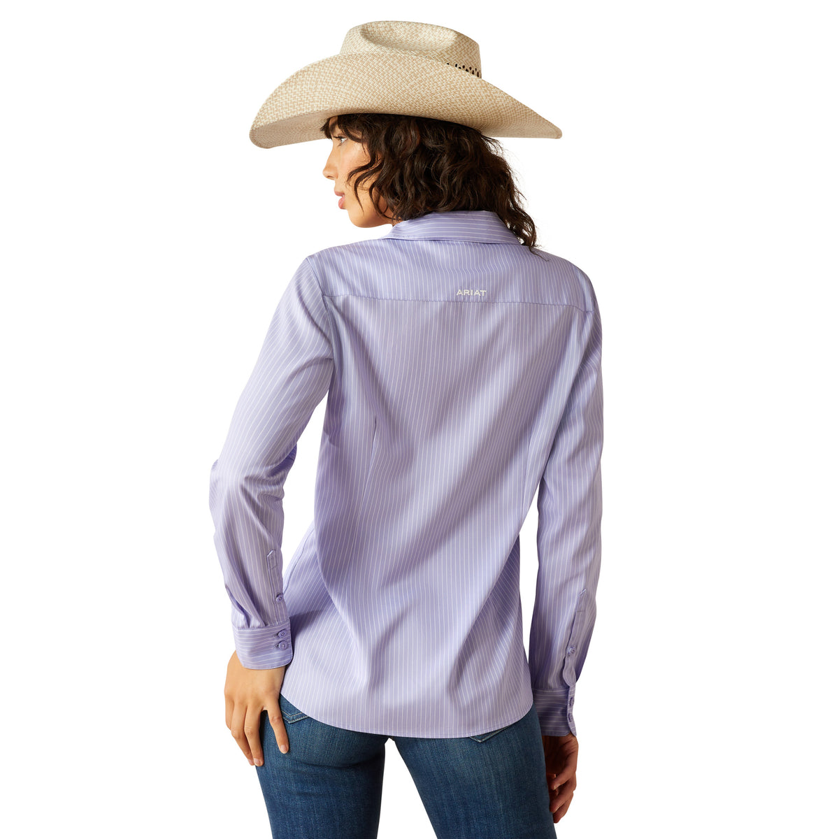 Ariat Women's Kirby Pro L/S Western Shirt. Woman wearing a light purple button-up shirt and blue jeans with a cowboy hat on a white background