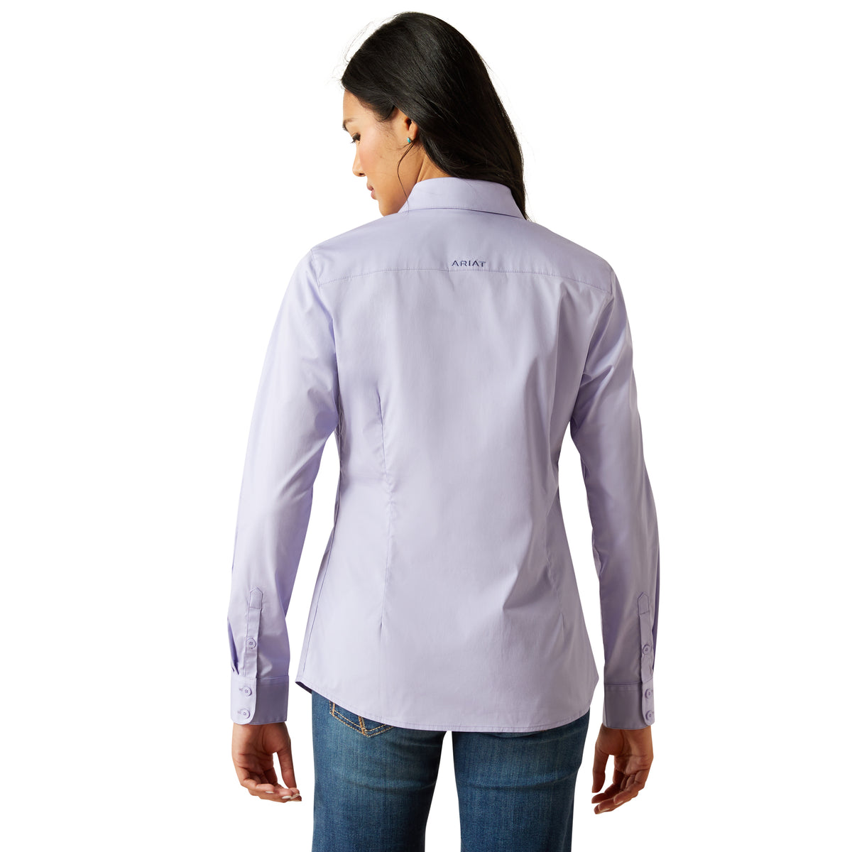 Ariat Women's Wrinkle Resistant Team Kirby L/S Western Shirt. Woman wearing a light purple shirt with a brand logo on the back, standing against a white background.