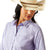 Ariat Women's Wrinkle Resistant Team Kirby L/S Western Shirt. Woman wearing a light purple shirt with 'Ariat' branding and a straw hat on a white background