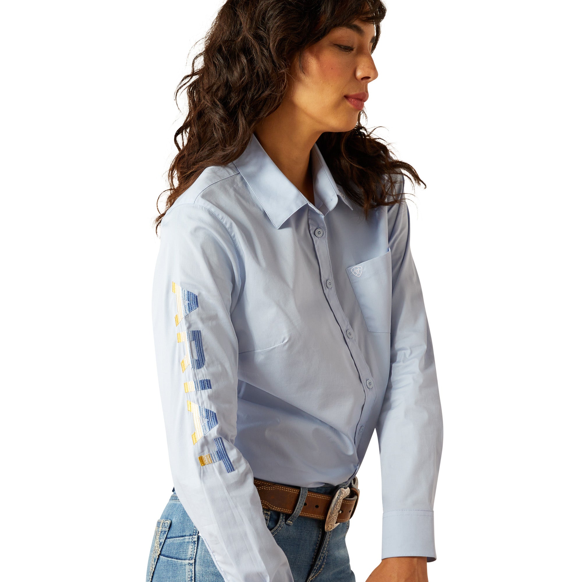 Ariat Women's Wrinkle Resistant Team Kirby Western Shirt. Woman wearing a light blue shirt with colorful patterns on sleeves against a white background