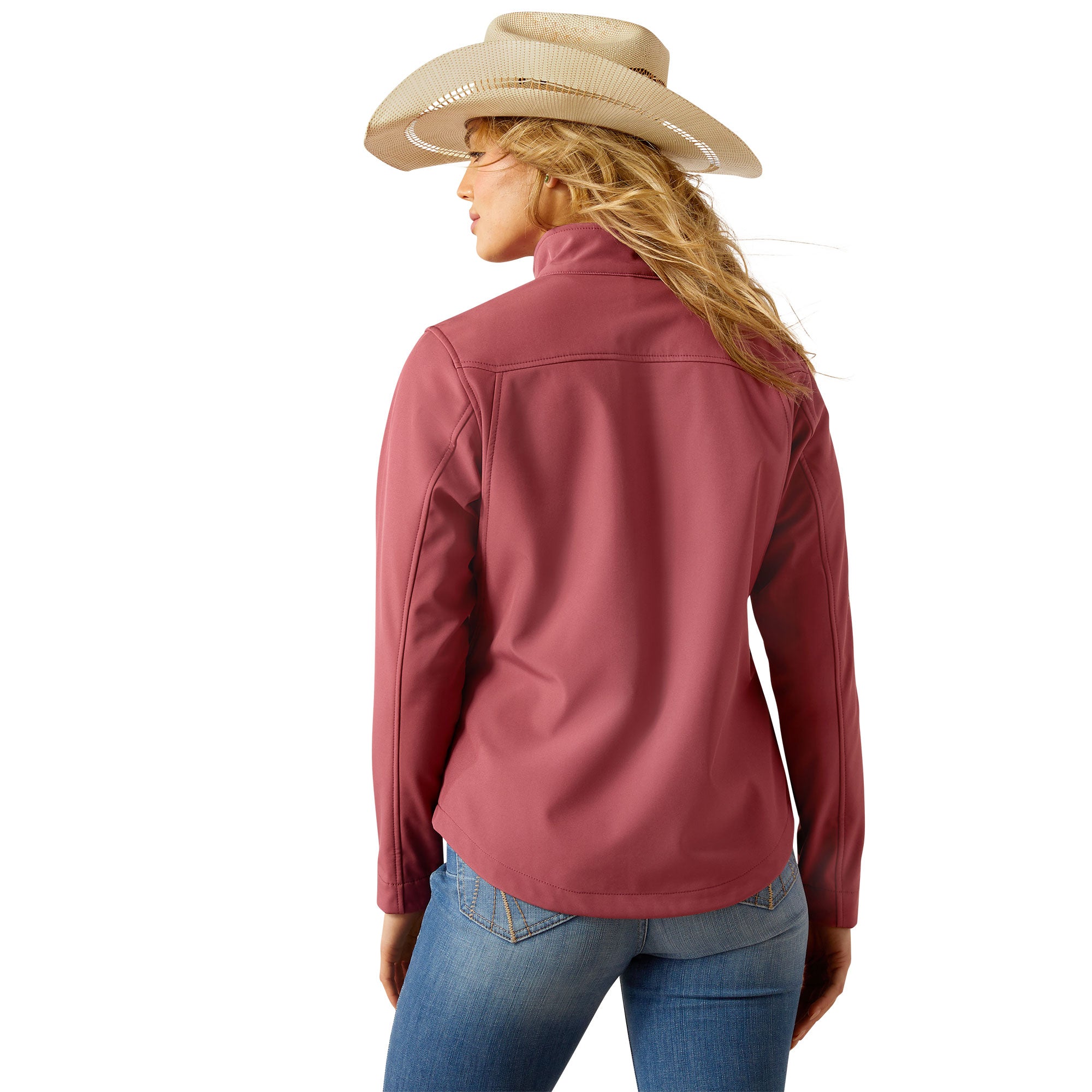 Ariat Women's Team Softshell Jacket. Woman wearing a pink jacket and blue jeans with a white background