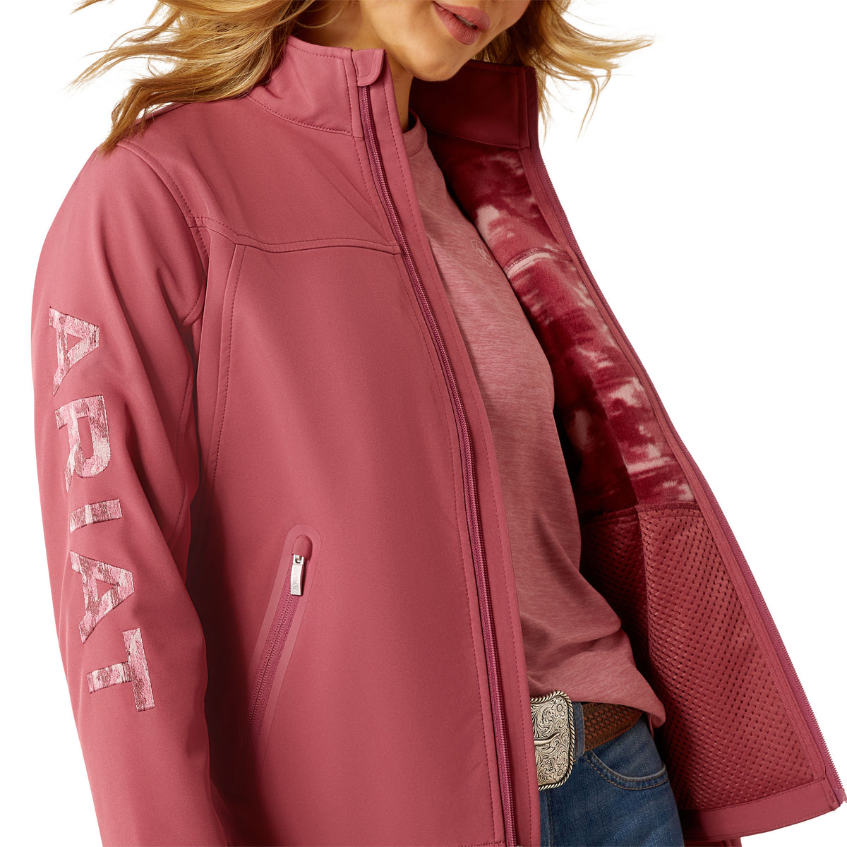 Ariat Women's Team Softshell Jacket. Pink jacket with 'Ariat' branding on sleeve, worn by a person.