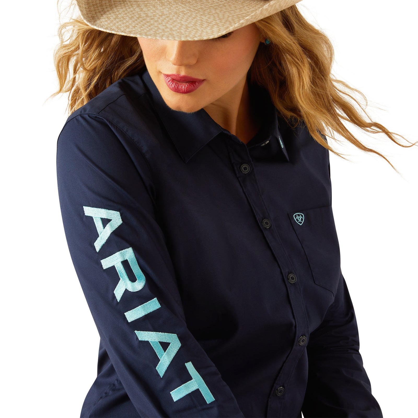 Ariat Women's Team Kirby Stretch L/S Western Shirt. Woman wearing a navy Ariat shirt, jeans, and a cowboy hat on a white background
