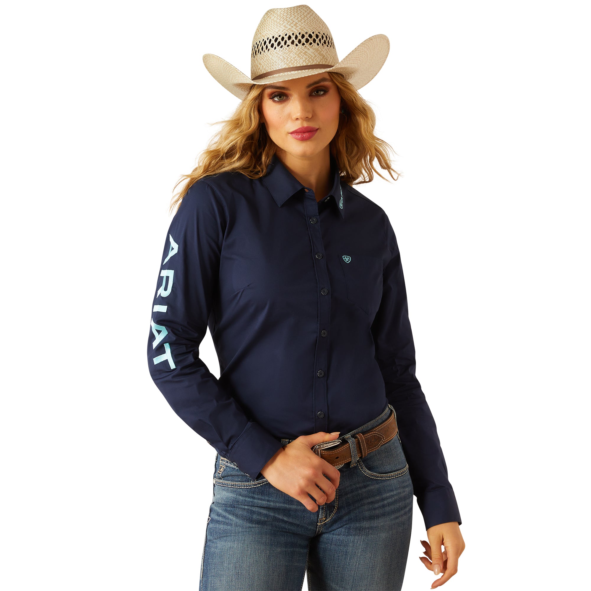 Ariat Women's Team Kirby Stretch L/S Western Shirt. Woman wearing a navy Ariat shirt, jeans, and a cowboy hat on a white background