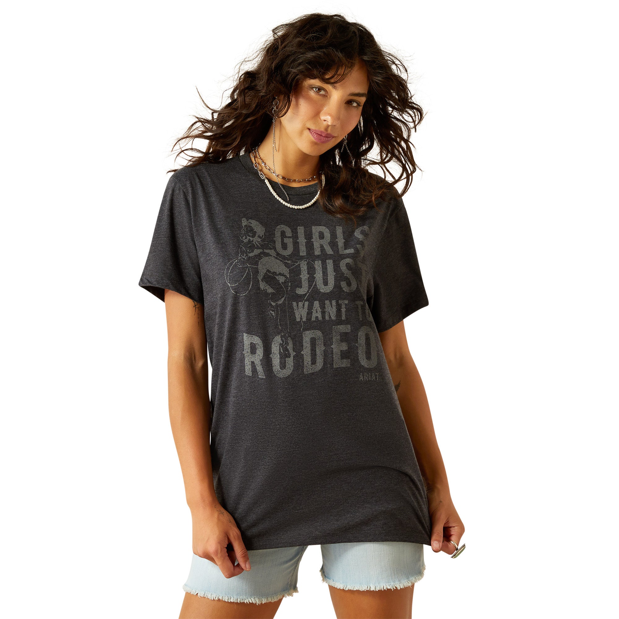 Àriat Women's Rodeo Girls T-Shirt. Woman wearing a dark gray t-shirt with text and light denim shorts, standing on a white background.