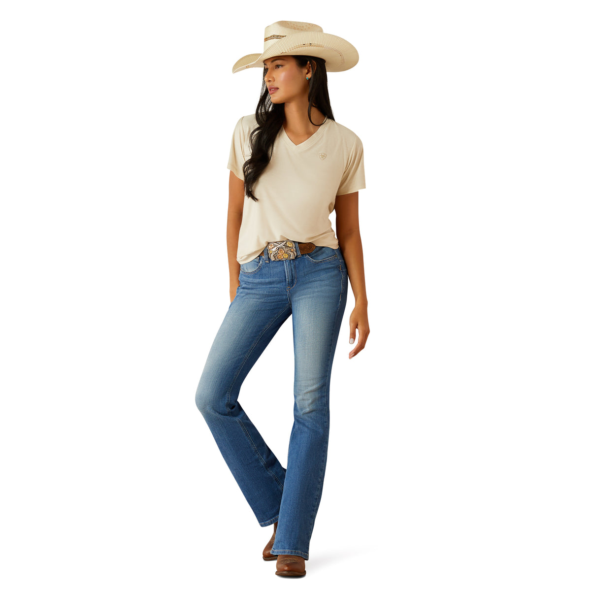 Ariat Women's Cassandra High Rise Boot Cut Jean. Woman wearing a beige shirt, blue jeans, and a cowboy hat on a white background