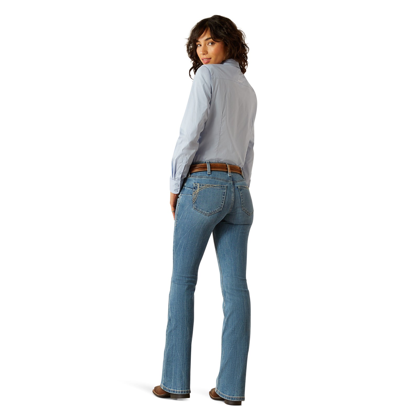 Ariat Women's Naz Perfect Rise Boot Cut Jean. A woman wearing Ariat Women's Naz Perfect Rise Boot Cut Jeans with a pair of boots and a blue shirt.
