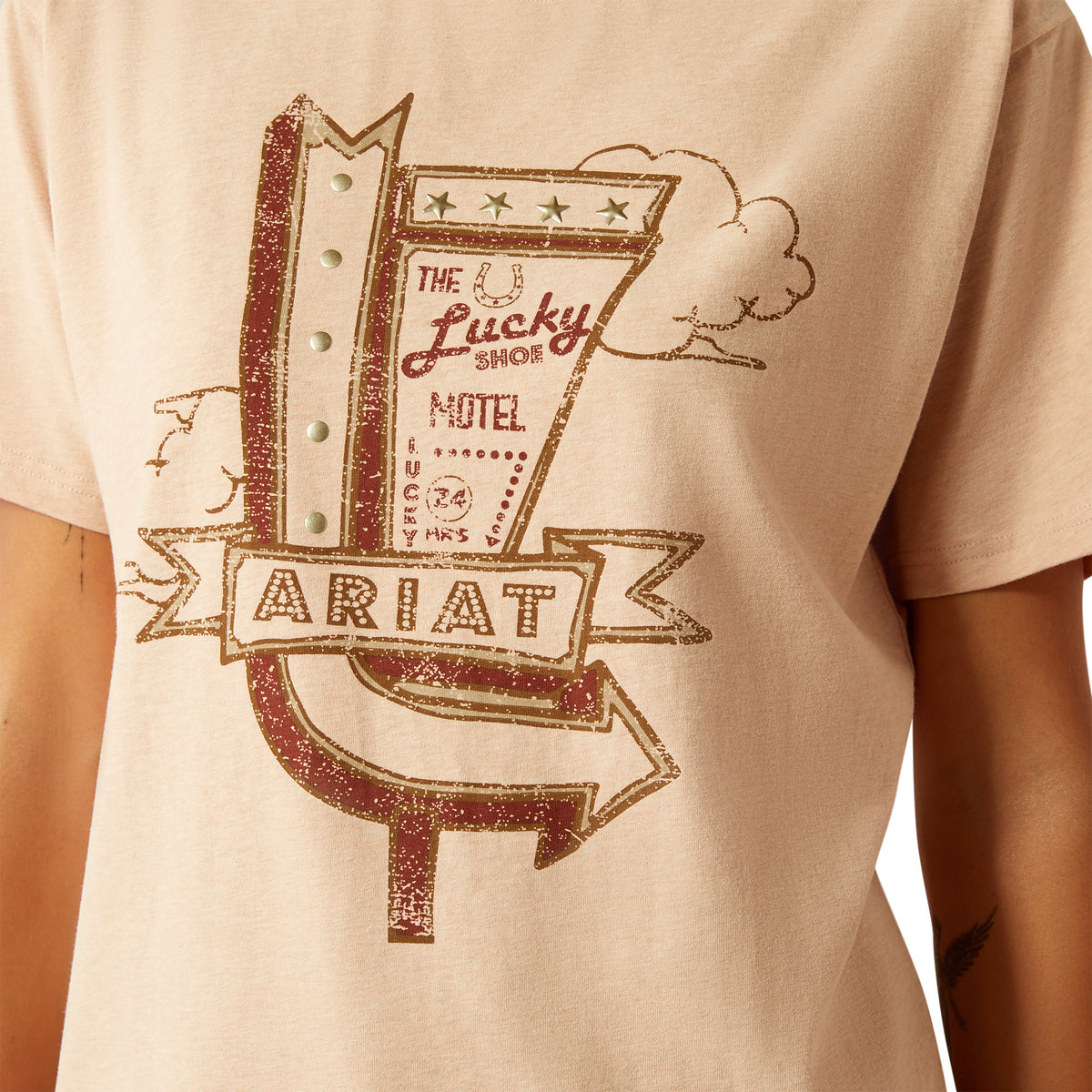 Ariat Women's Roadside T-Shirt. Beige t-shirt with a graphic design of 'The Lucky Shoe Motel' and 'Ariat' on a plain background