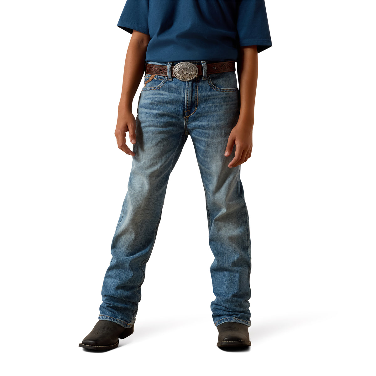 A model from the waist down wearing a pair of medium-wash blue denim jeans with a brown leather belt featuring a large silver buckle, paired with a blue shirt and brown boots, on a white studio background.