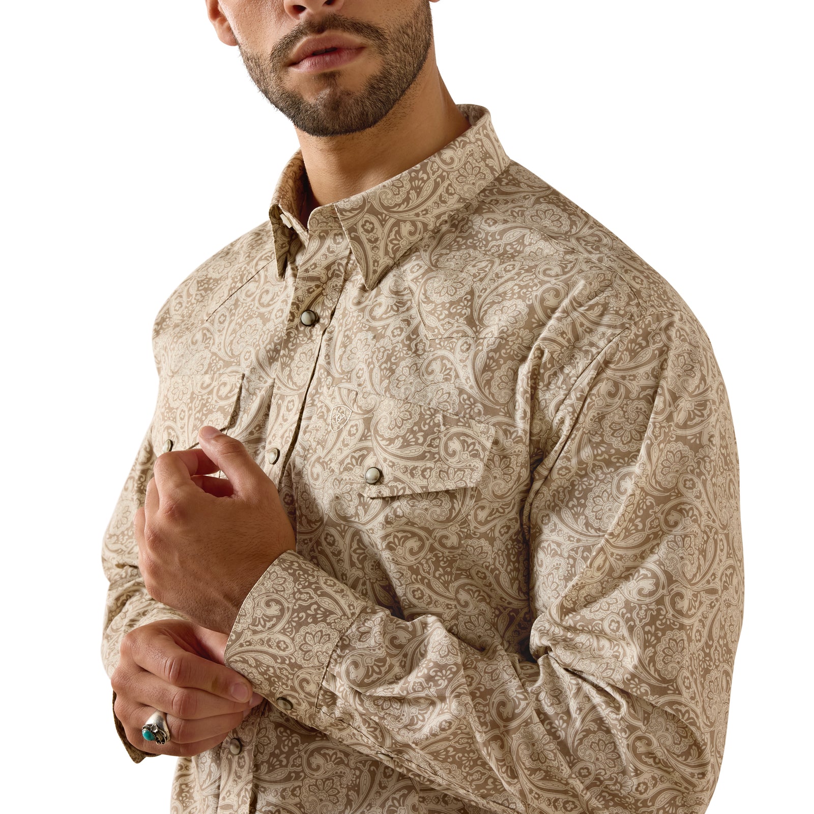 A man wearing a beige and brown paisley patterned long-sleeve button-down shirt, shown from the chin down against a plain white background.